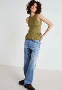 Top peplum en verde oliva de punto acanalado, combinado con jeans rectos desgastados de color azul claro y zuecos marrones. Diseño sencillo, sin patrones.