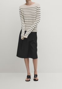 Maglione a righe beige e nero con maniche lunghe, abbinato a una gonna nera lunga fino al ginocchio e sandali neri con fasce larghe.