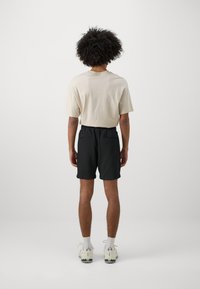 Beige cotton t-shirt with a relaxed fit and short sleeves, paired with black shorts featuring two back pockets. White sneakers complete the look.