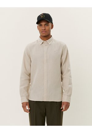 Beige Langarm-Hemd aus Leinen mit Kragen, durchgehendem Knopfverschluss und strukturierter Oberfläche. Getragen mit vertikal gestreiften Hosen.