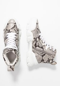 Sneakers typu high-top w beżowym i czarnym wzorze wężowym. Posiadają białe sznurówki, boczny zamek oraz masywną białą podeszwę.