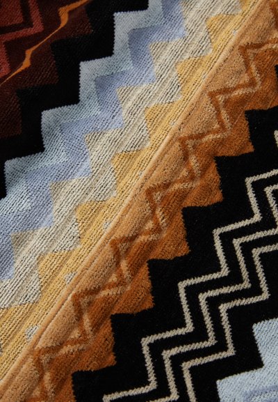 Tappeto tessuto ad area con un motivo a zigzag in tonalità terre, tra cui ruggine, blu, beige e nero, con una superficie morbida e testurizzata.