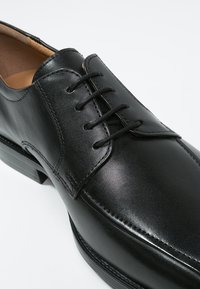 Chaussure habillée en cuir noir à finition lisse, dotée d'un design classique à lacets et d'une forme légèrement allongée. Talon robuste avec un minimum de détails.