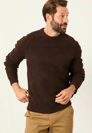Brauner gerippter Pullover mit Rundhalsausschnitt, langen Ärmeln und strukturiertem Stoff. Tragen mit beigen Hosen, die einen lockeren Schnitt haben.