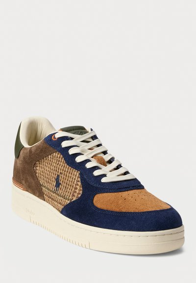 Sneaker with a brown suede upper, navy blue accents, textured tan fabric panel, green heel tab, white laces, and a cream rubber sole.