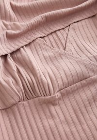 Tissu côtelé rose doux avec un détail froncé et une couture en forme de V sur un vêtement, soulignant la texture et la construction.