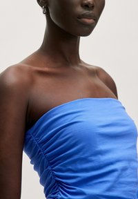 Blauwe katoenen strapless top met verzamelde zijkanten voor een textuuraccent, gecombineerd met zilveren creolen. Glad materiaal en een aansluitend design.