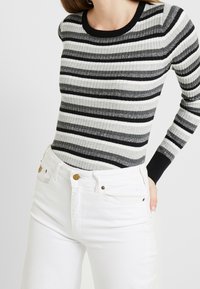 Szary i czarny prążkowany sweter z okrągłym dekoltem, w połączeniu z białymi, wysokim stanem dżinsami z detalami w kolorze złota.