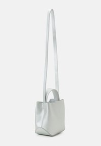 Mała srebrna skórzana torba typu worek z długim paskiem na ramię i krótką rączką, stojąca pionowo na białym tle.