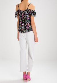 Mustat olkaimeton kukkamekko, jossa on kirkkaanvärisiä kukkia. Yhdistetty valkoisiin leveisiin housuihin ja vaaleanpunaisiin korkokenkiin.