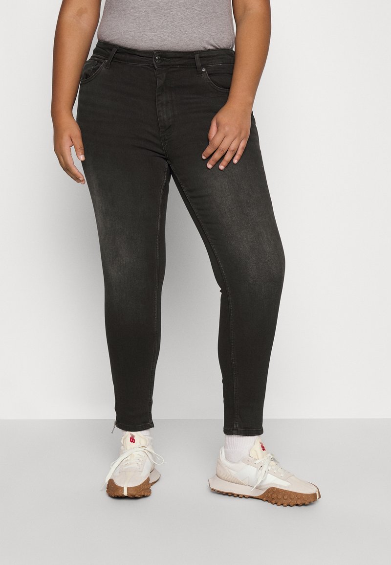 Zwarte skinny jeans van denim met voorzakken, een ritssluiting en een aansluitend ontwerp. Draagt witte sportschoenen en een grijs T-shirt.