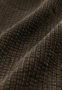 Texturovaná tkanina v tmavě hnědé barvě, se žebrovaným vzorem a měkkými, vystouplými sekcemi a jemnou hloubkou. Ideální pro oděvy nebo čalounění.