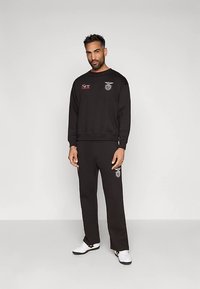 Conjunto de sweatshirt e calças pretas feito de algodão. Sweatshirt apresenta um logótipo e texto no peito; as calças têm o logótipo correspondente. Ténis brancos completam o visual.