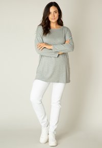 Graue Langarm-Tunika mit rundem Ausschnitt, kombiniert mit weißen Slim-Fit-Hosen und weißen Sneakers. Weicher Stoff mit seitlichen Schlitzen am Saum.