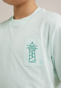 Gaiši zila kokvilnas T-krekla ar za�ļu izšuvumu bākas attēlā. Audumam ir gluda tekstūra un apaļas kakla dizains.