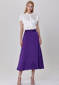 Blouse blanche en satin à manches courtes avec des boutons, associée à une jupe large violette dotée d'une ceinture. Le tissu est lisse avec un design fluide.