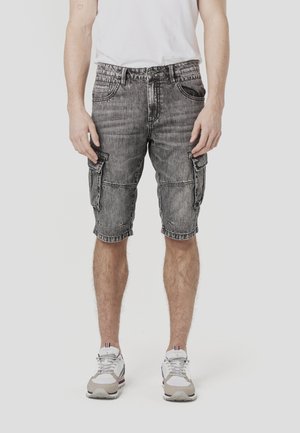 Cargo-Shorts aus abgenutztem grauem Denim, knielang mit mehreren Taschen und einem lässigen Schnitt. Kombiniert mit weißen und grauen Sportschuhen.