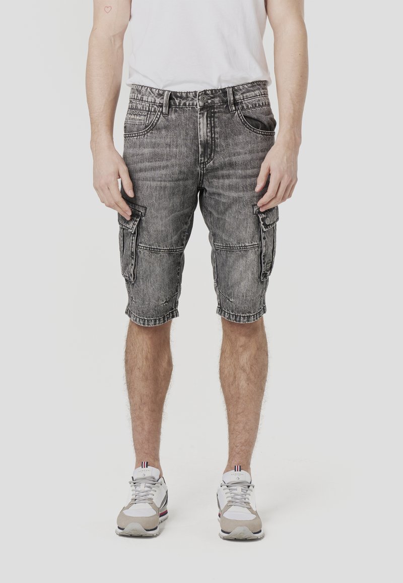 Shorts cargo en denim gris usé, longueur genou avec plusieurs poches et une coupe décontractée. Portés avec des chaussures de sport blanches et grises.