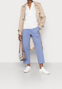 Beige trenchcoat over en hvid striped skjorte, blå cropped bukser, hvide sneakers og en lille grå håndtaske med rem.