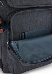 Mörk denimryggsäck med en dragkedjeficka med en teal-fodring, flera inre fack och en texturerad tygyta.