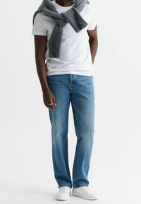 Camiseta blanca, jeans de mezclilla azul, bufanda de punto gris caída sobre los hombros, zapatillas blancas, corte holgado, tejido de peso medio, estilo casual.