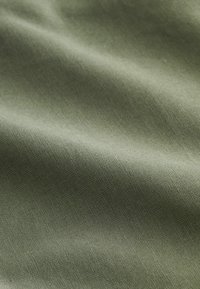 Prim-plan al unei țesături netede, verde măsliniu, cu pliuri moi și o textură subtilă ce evidențiază un model fin de țesătură.