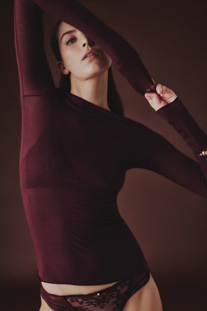 Weinrotes Langarmoberteil aus weichem, dehnbarem Stoff mit figurbetontem Design und Ausschnitten an den Ärmeln, kombiniert mit Unterteilen mit Spitzenakzenten.