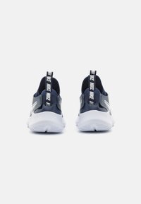 Chaussures Nike avec une tige bleu marine, une semelle blanche et des accents texturés. Présente une languette avec logo et un design à enfiler.