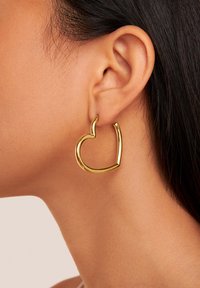 Pendiente de aro en forma de corazón dorado, metal pulido con un acabado suave. Presenta un acento puntiagudo en la parte superior, diseño ligero para un uso cómodo.