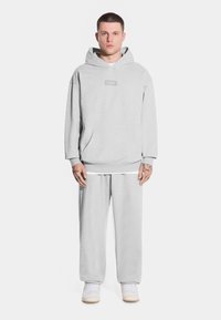 Szary hoodie z kieszenią kangurką i małym logo z przodu, zestawiony z luźnymi spodniami dresowymi w tym samym kolorze. Wykonany z mieszanki bawełny, w luźnym fasonie.