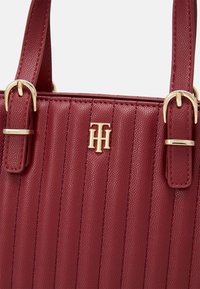 Rote strukturierte Handtasche mit vertikalen Rippungen, goldfarbenen Beschlägen und einem Logo-Akzent. Verfügt über stabile Griffe und eine glatte Oberfläche.