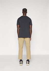 Black short-sleeve t-shirt, relaxed fit, paired with beige trousers and sneakers featuring dark and light accents.