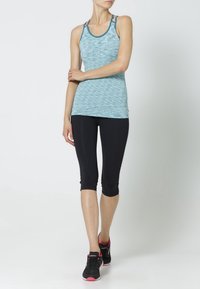 Jasnoniebieski sportowy top na ramiączkach z teksturowanym wzorem, zestawiony z czarnymi legginsami capri, uzupełniony czarno-różowymi butami sportowymi.