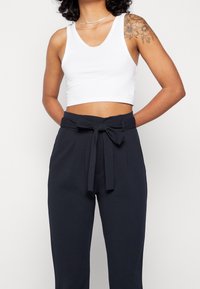 Top court blanc à décolleté en V, associé à un pantalon marine taille haute avec ceinture à nouer et détail plissé sur le devant.