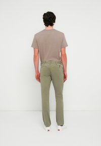 Ανοικτό καφέ κοντομάνικο μπλουζάκι, ελαιί πράσινο παντελόνι με πίσω τσέπες και λευκά αθλητικά παπούτσια. Απλός σχεδιασμός με εστιασμένη χρωματική παλέτα.