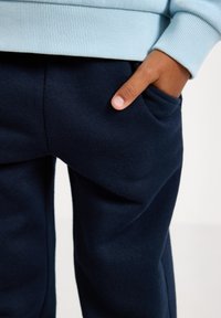 Marineblauwe sweatpants met een gladde textuur en een zijzak, gecombineerd met een lichtblauwe sweatshirt, voorzien van ribgebreide manchetten en tailleband.