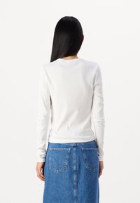 Maglietta bianca a maniche lunghe in tessuto ribbed con scollo tondo, indossata con una gonna di jeans a taglio dritto e due tasche posteriori.