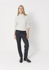 Grå ribbad polo tröja med avslappnad passform, i kombination med mörkgrå dragbandsbyxor med sidofickor och silverfärgade detaljer. Svarta ankelstövlar.