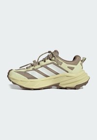 Beige and brown trail running shoe with thick sole, rugged tread, elastic laces, and three white side stripes.