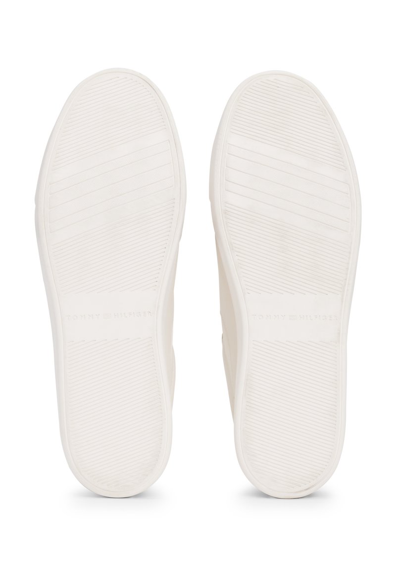 Semelles en caoutchouc blanc avec des motifs de grip texturés, comportant des lignes horizontales et verticales. Logo "TOMMY HILFIGER" embossé près du talon.