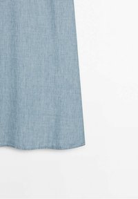 Tessuto in denim azzurro chiaro appeso su uno sfondo bianco, che mostra l'orlo inferiore con cuciture visibili.