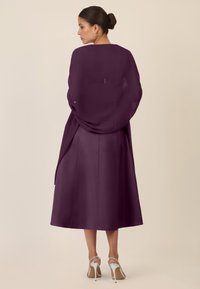 Langes lila Kleid aus fließendem Stoff mit einem schlichten Design. Verfügt über eine taillierte Taille und einen leicht ausgestellten Saum. Getragen mit silbernen Absatzsandalen.
