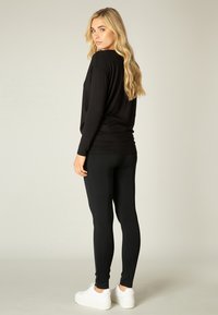 Zwarte long-sleeve top met een relaxte fit, gecombineerd met zwarte legging en witte platform sneakers, met een slank ontwerp en een gladde textuur.