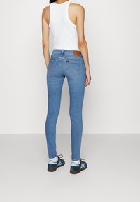 Modré úzké džíny s vysokým pasem, vybavené koženou značkovou nášivkou, zadními kapsami a jemně vybledlým vzhledem. Doplňuje je černé a modré tenisky.