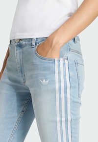 Svetlomodré džínsy s bielym trojpruhovým dizajnom po stranách a malou bielou nášivkou. Úzky strih so prednými vreckami a kovovým gombíkom.
