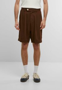 Braune, gefaltete Shorts mit Knopfverschluss, knielang, aus weichem Material. Entworfen mit einem lockeren Schnitt und umgeschlagenem Saum.