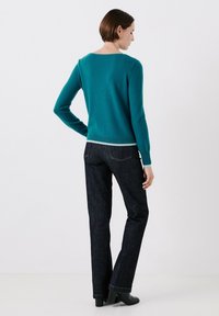 Maglione di lana color turchese con scollatura ampia, indossato su jeans blu scuro. Il maglione ha maniche aderenti e una banda chiara a contrasto sull'orlo.