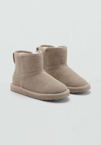 Botines de ante beige con puntera redonda, forro suave y suelas de goma planas; cuentan con un puño doblado y una lengüeta en la parte posterior.
