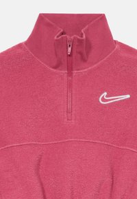 Ružový fleecový pulóver s polovičným zipsom. Mäkká textúra s rebrovaným golierom. Na ľavej strane hrudníka je biele logo Nike. Jednoduchý dizajn bez vzorov.