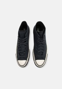 Mustad kõrgetop sneakers mustast kanvasest, valge kummist varba ja tallaga. Omab lamedaid musti paelu ja tekstuurset viimistlust. Õrn brändimine tallal.